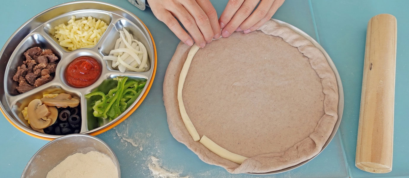 피자를 만드는 손과 오른쪽에는 토핑 재료가 있다.