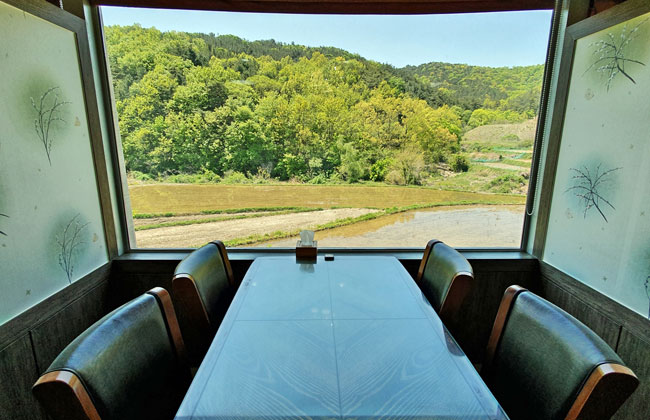 식당 내부에서 큰 창으로 푸른 산과 논이 보인다.