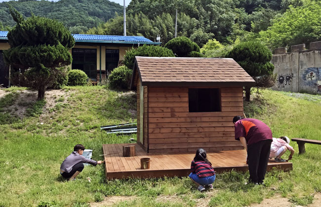 오두막에 코팅 페인트를 칠하는 아이들