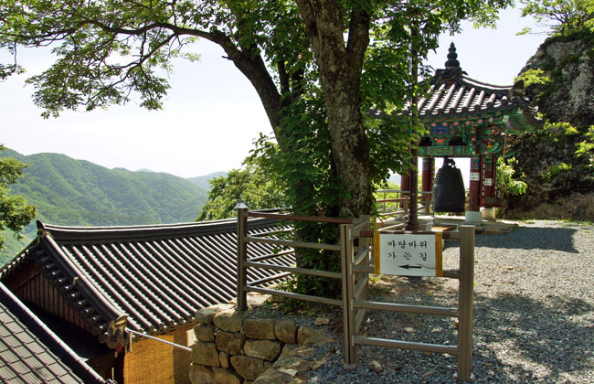 마당바위 가는 길 안내팻말 뒤로 주사암의 범종이 보인다.